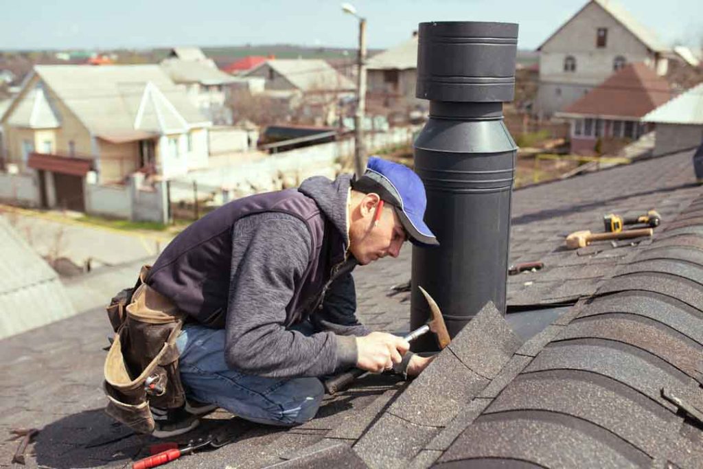 Professional Roofer with Hammer Repairing Asphalt Shingle Roof