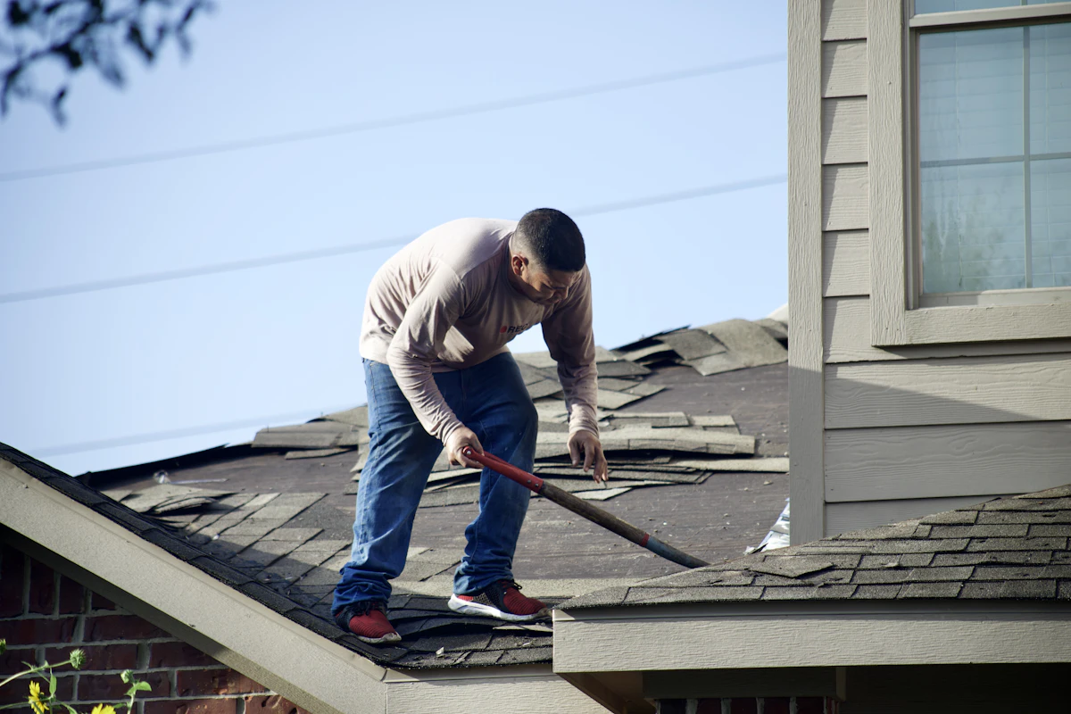Roofer performing shingle repair with a hammer on a residential roof