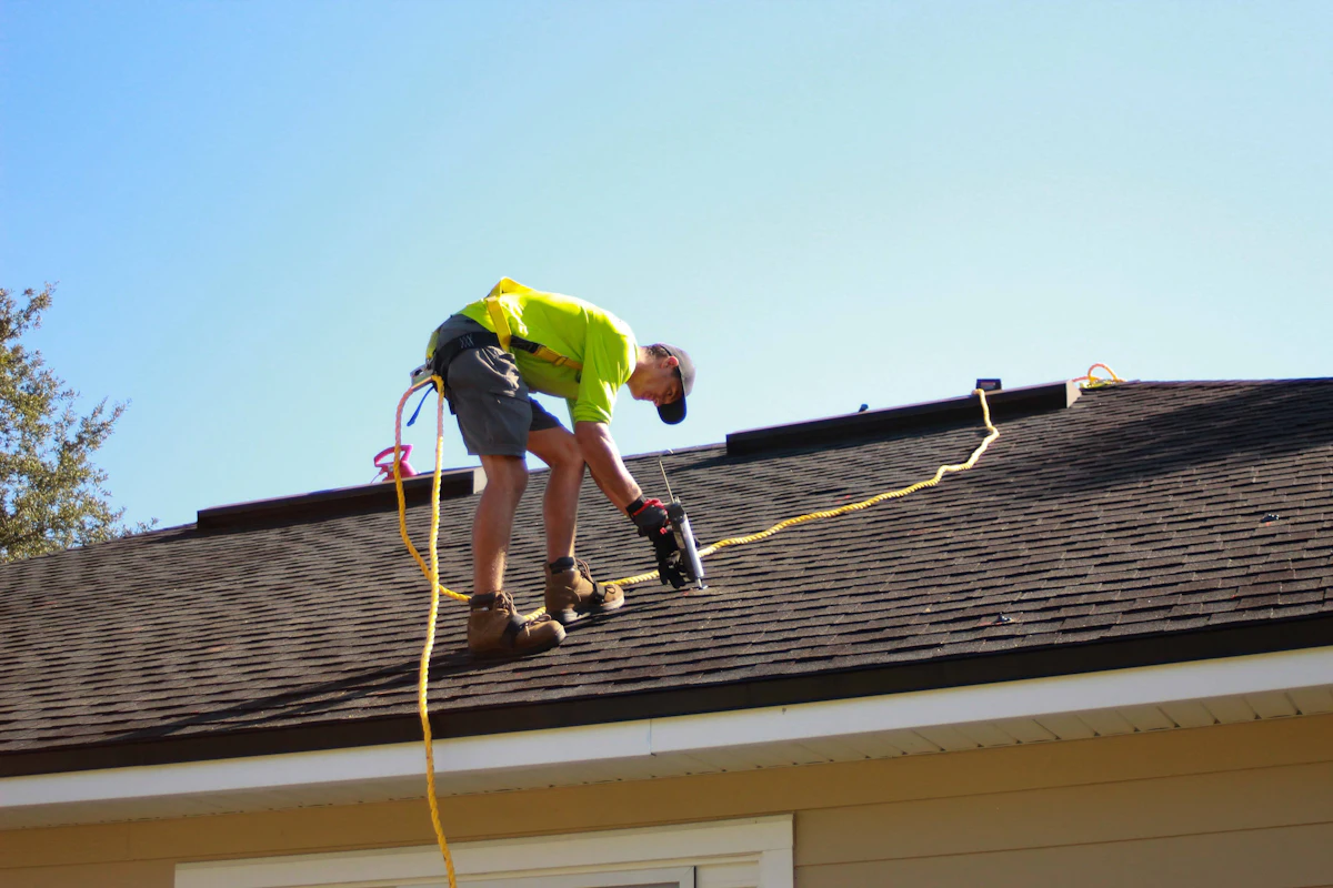 Professional roofer installing shingles with a drill on a residential roof